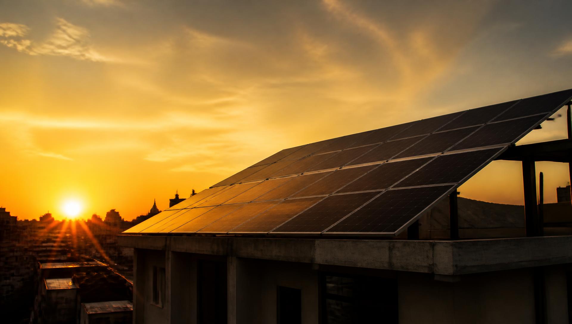 Rooftop solar array silhouetted against a golden sunset